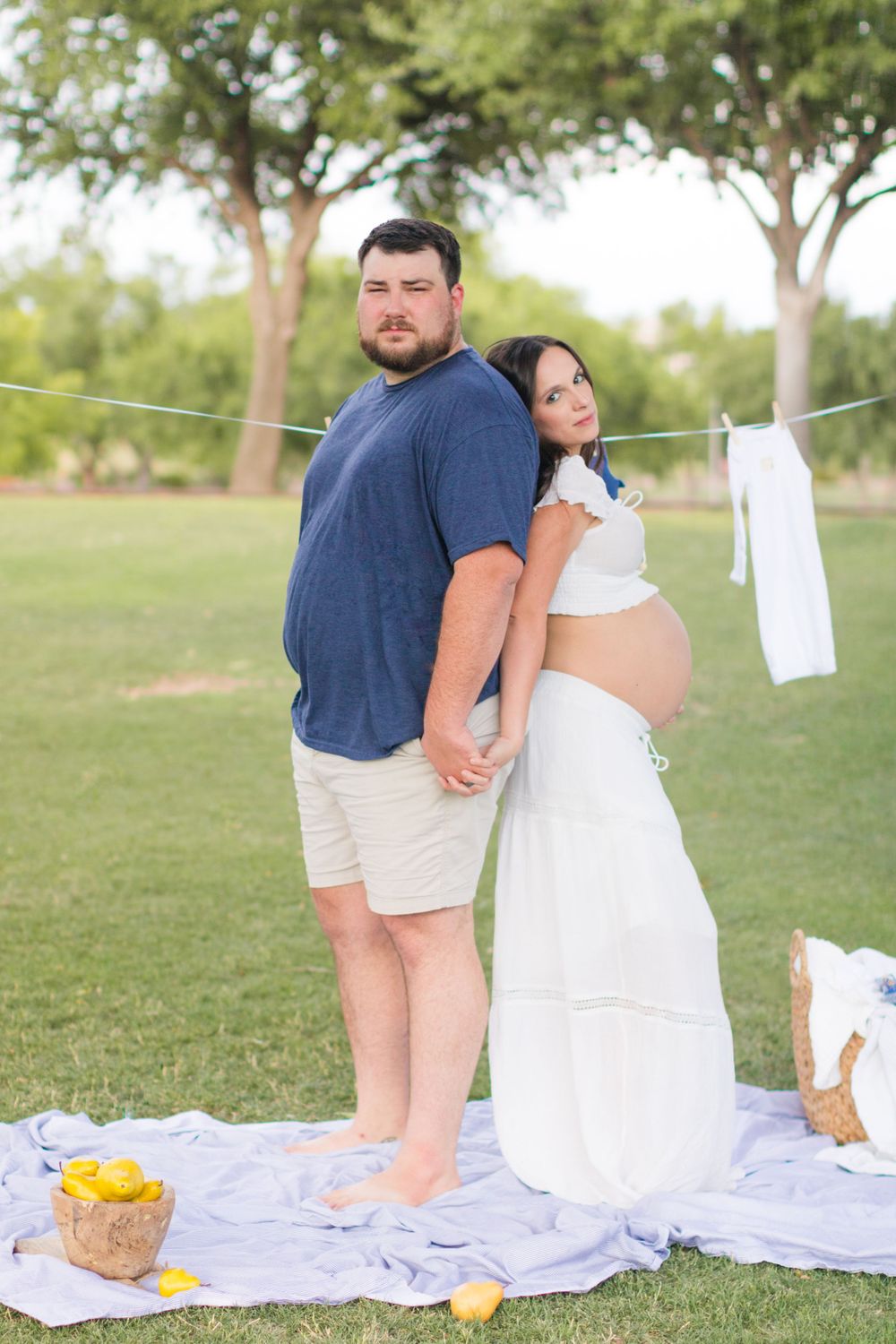 An expectant couple stand back to back, gazing at the camera.
