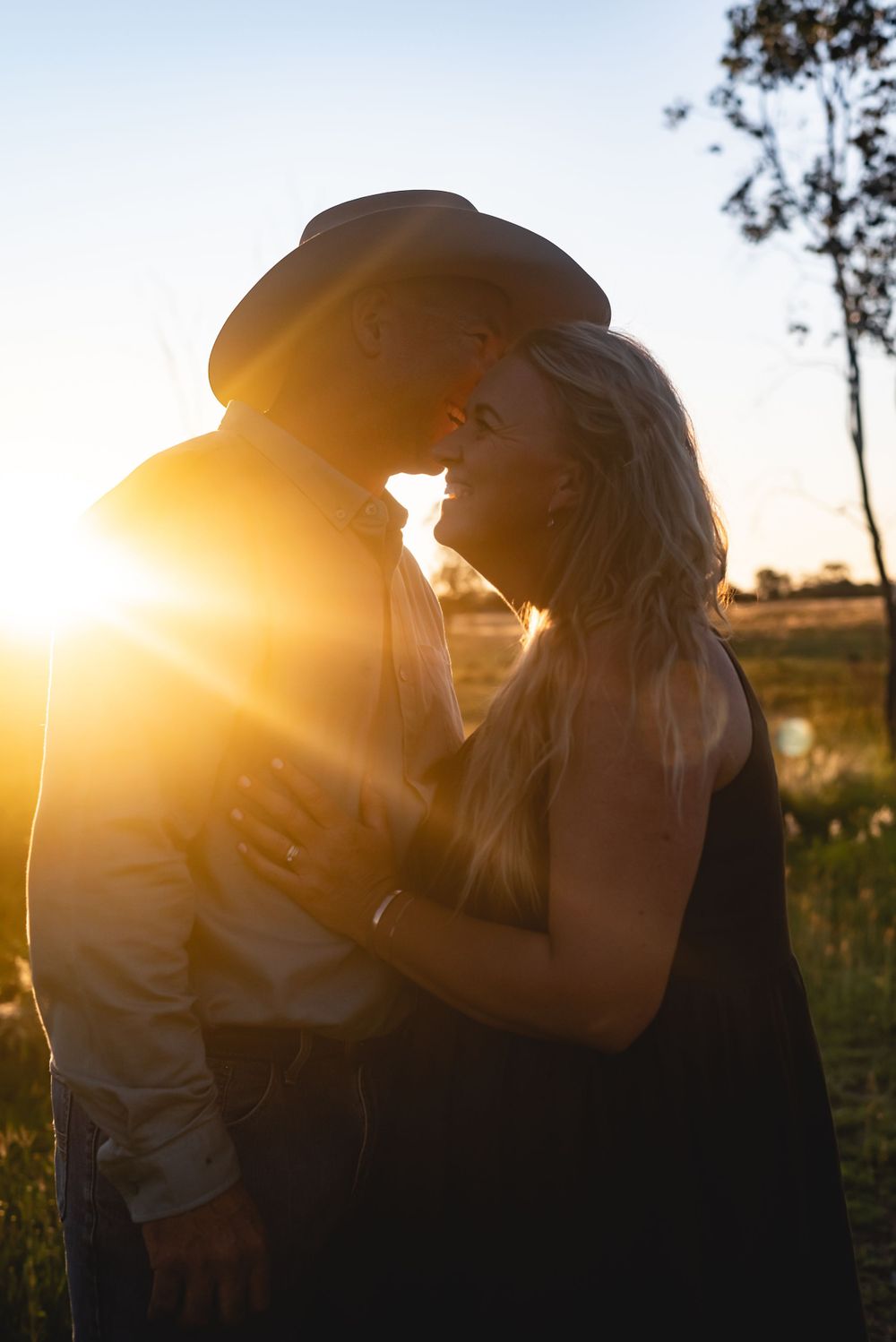 Romantic couple embracing in sunlit field during golden hour.
