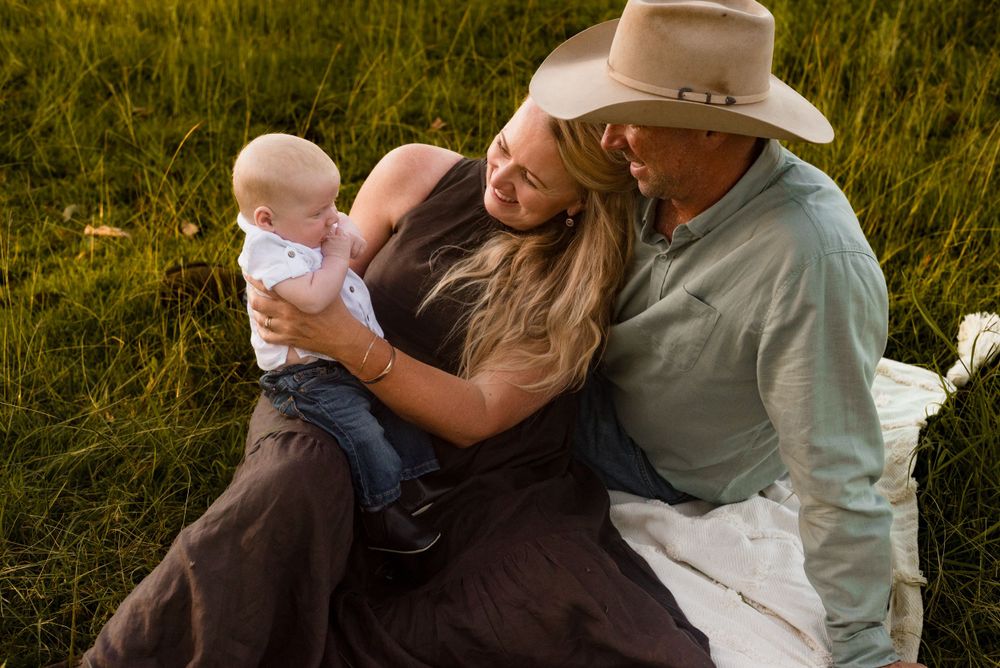Family shares tender moment together on blanket in sunlit field.