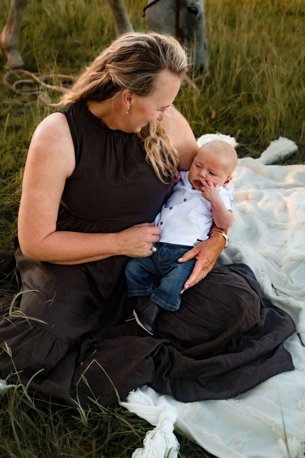 Parent and baby sharing tender moment on blanket in grassy field.