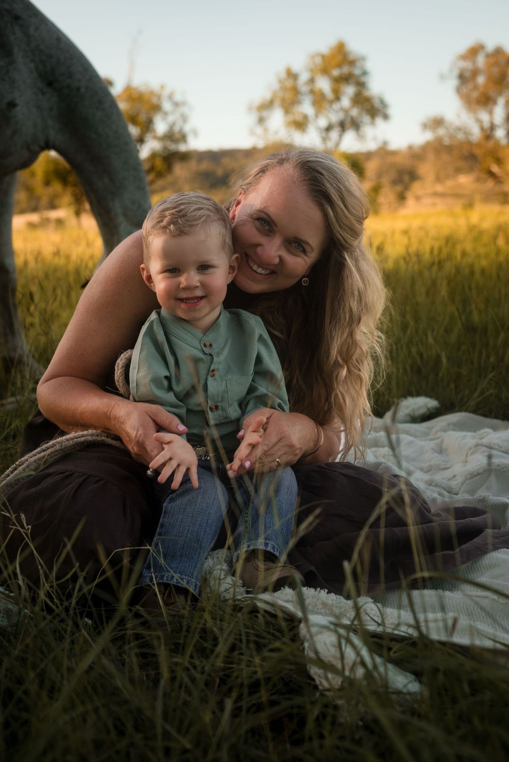 Mother and child share a joyful moment while sitting on blanket in grassy field.