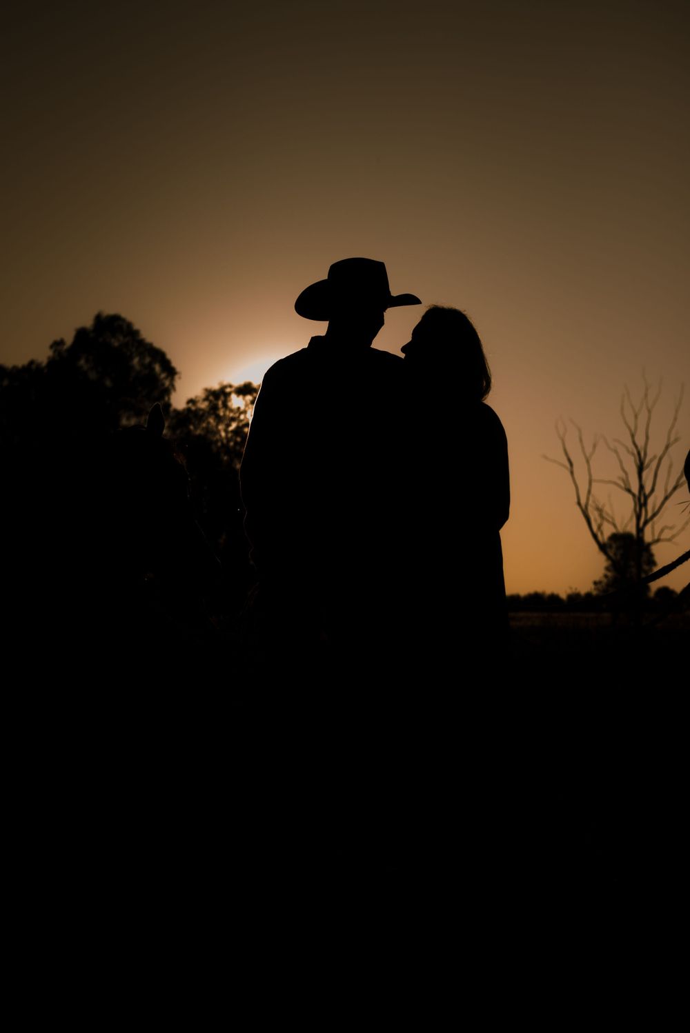 Silhouette of a couple in cowboy attire against a sunset sky.
