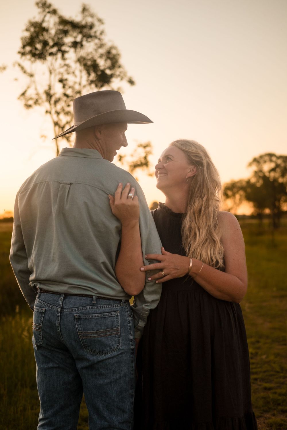 Couple shares intimate moment in countryside setting during golden hour.