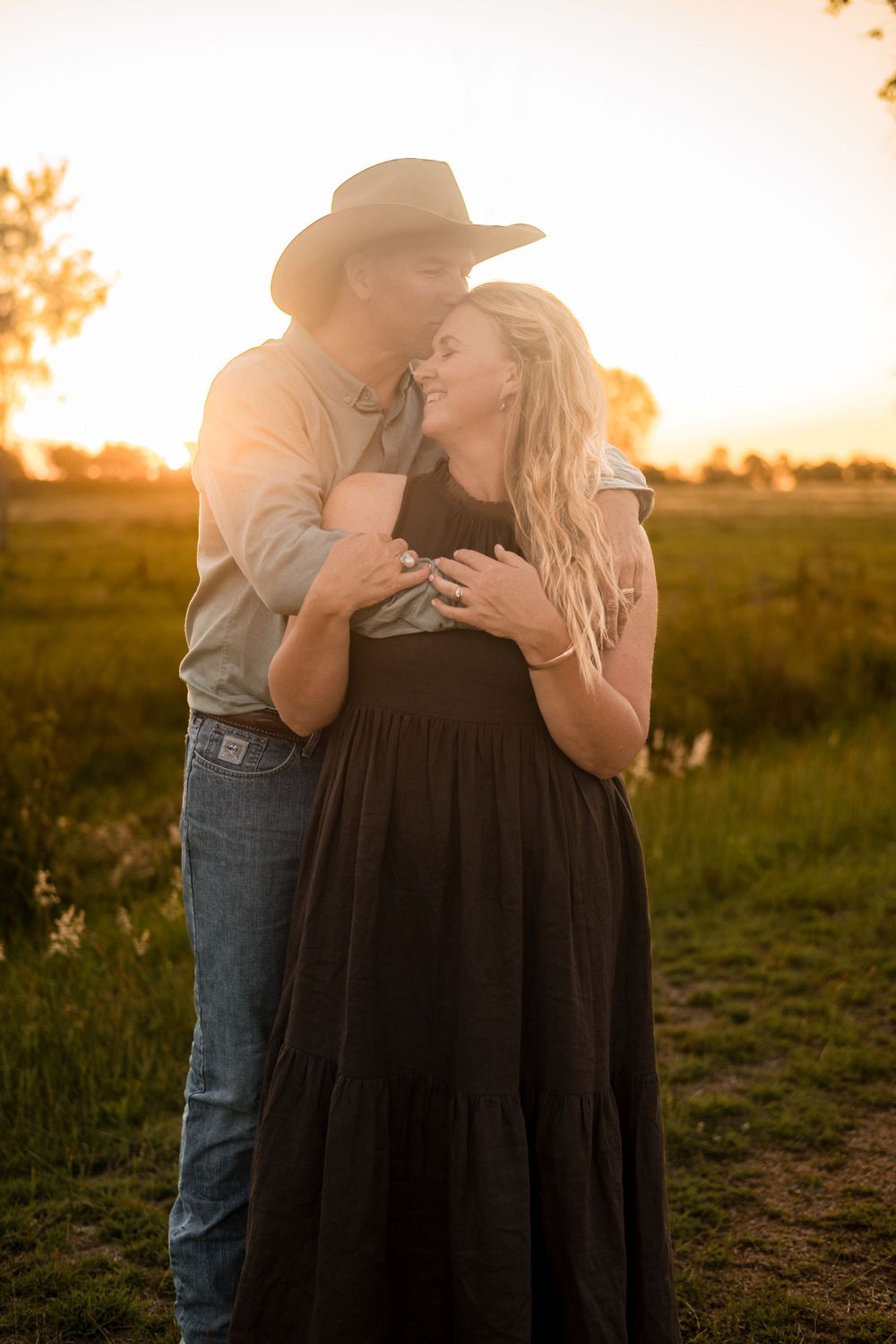 Romantic couple embrace in golden sunset light on rural farmland.
