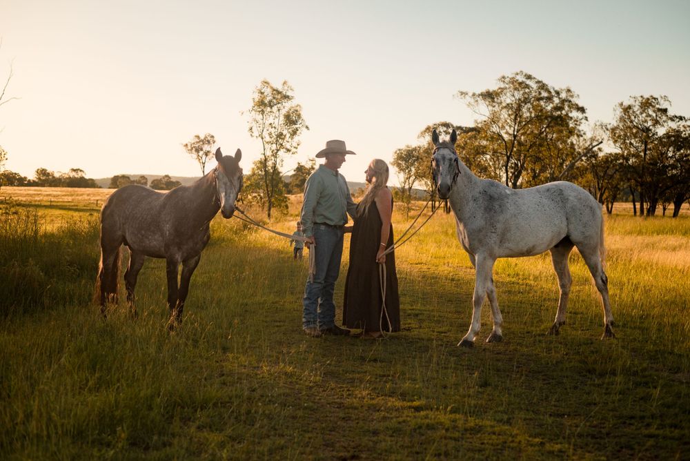 Family poses with their horses in a golden rural field during sunset.