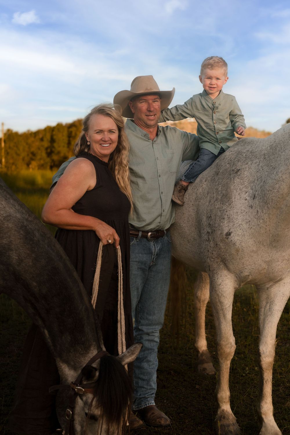 Family poses with horses on their ranch as young child sits atop a white horse.