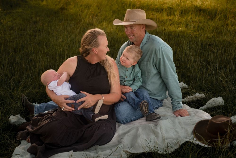 Family relaxing on a blanket in a grassy field during golden hour.