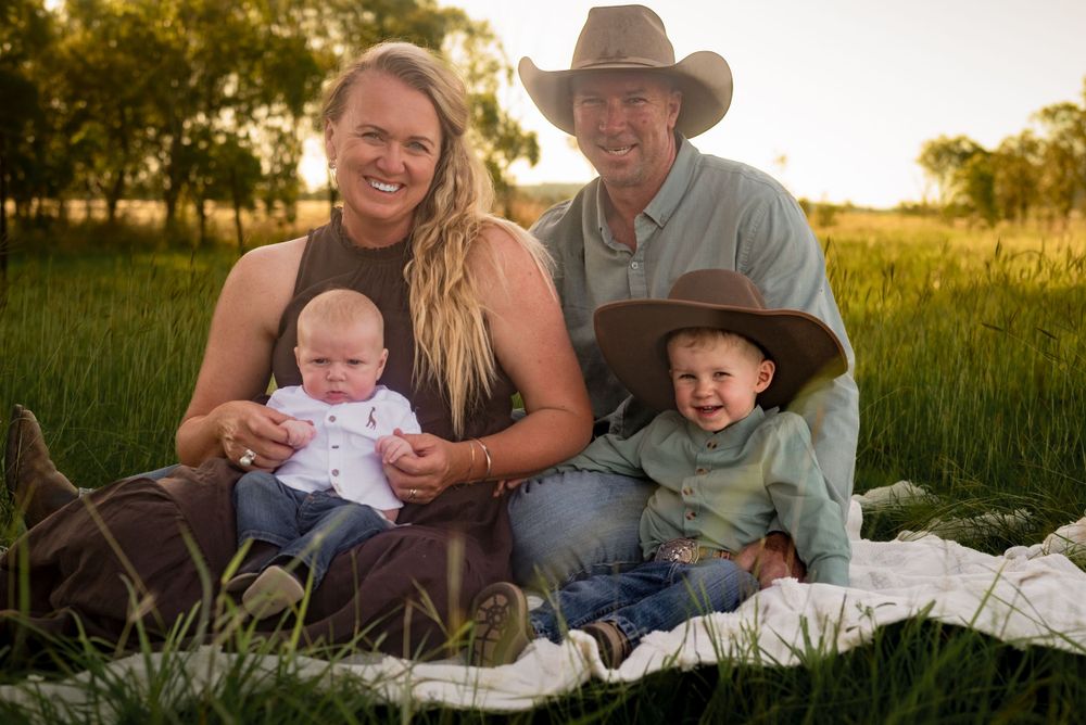 Family of four sits together on blanket in rustic field during sunset photoshoot.