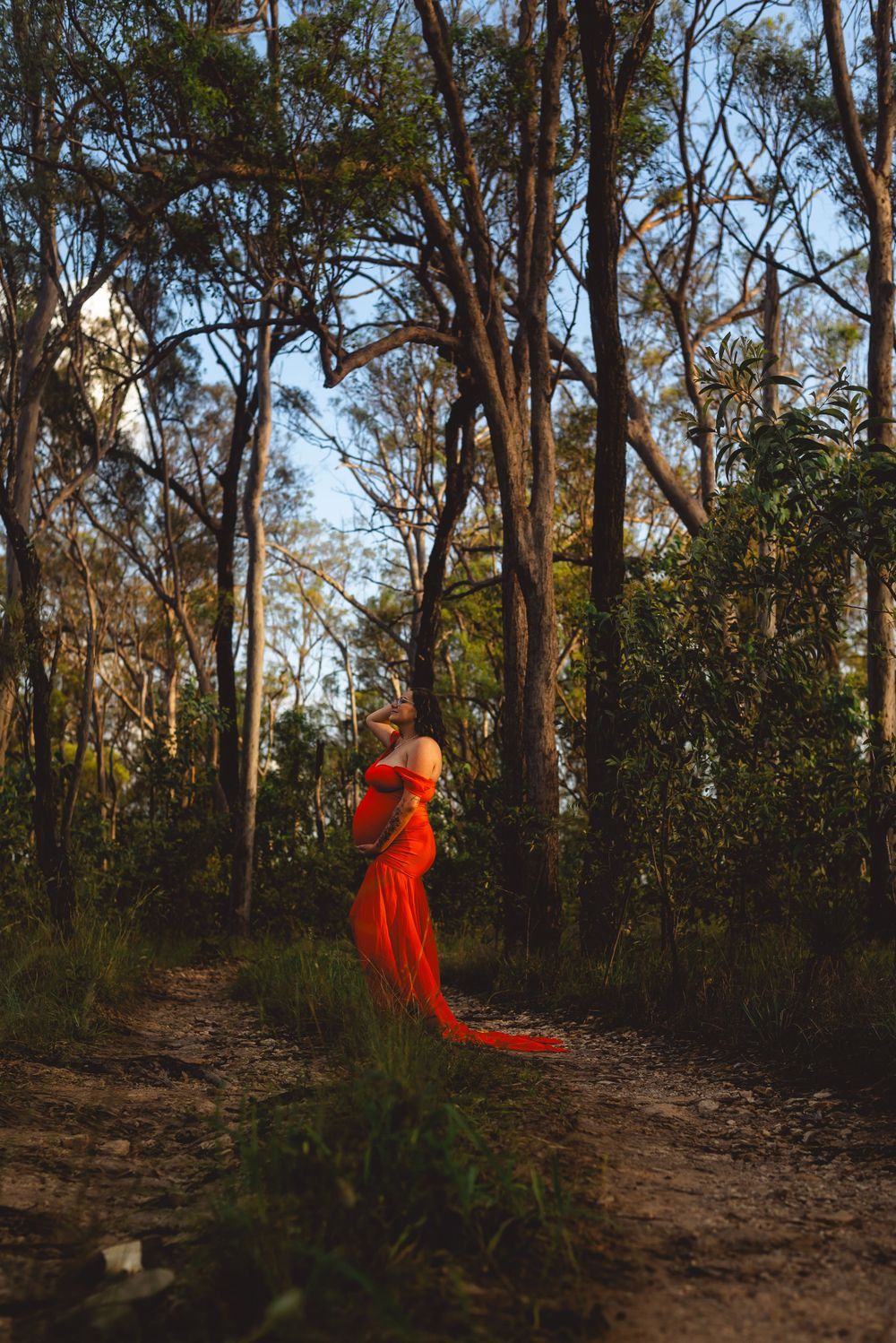 A person in a flowing red dress stands among tall eucalyptus trees in a forest setting.