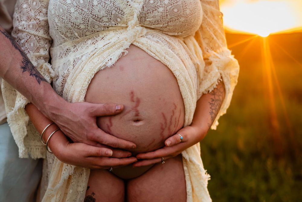 Close-up of hands cradling pregnant belly in lace dress during golden hour sunset photoshoot.