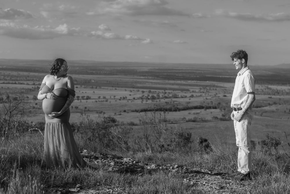 Dramatic black and white landscape maternity photo with couple standing on hilltop.