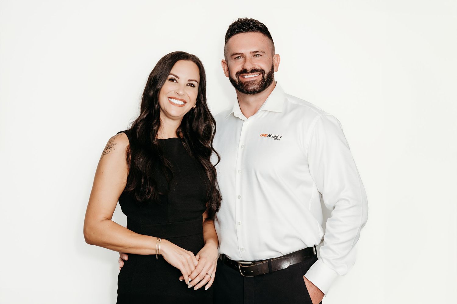 Professional couple poses together against white background in business attire.