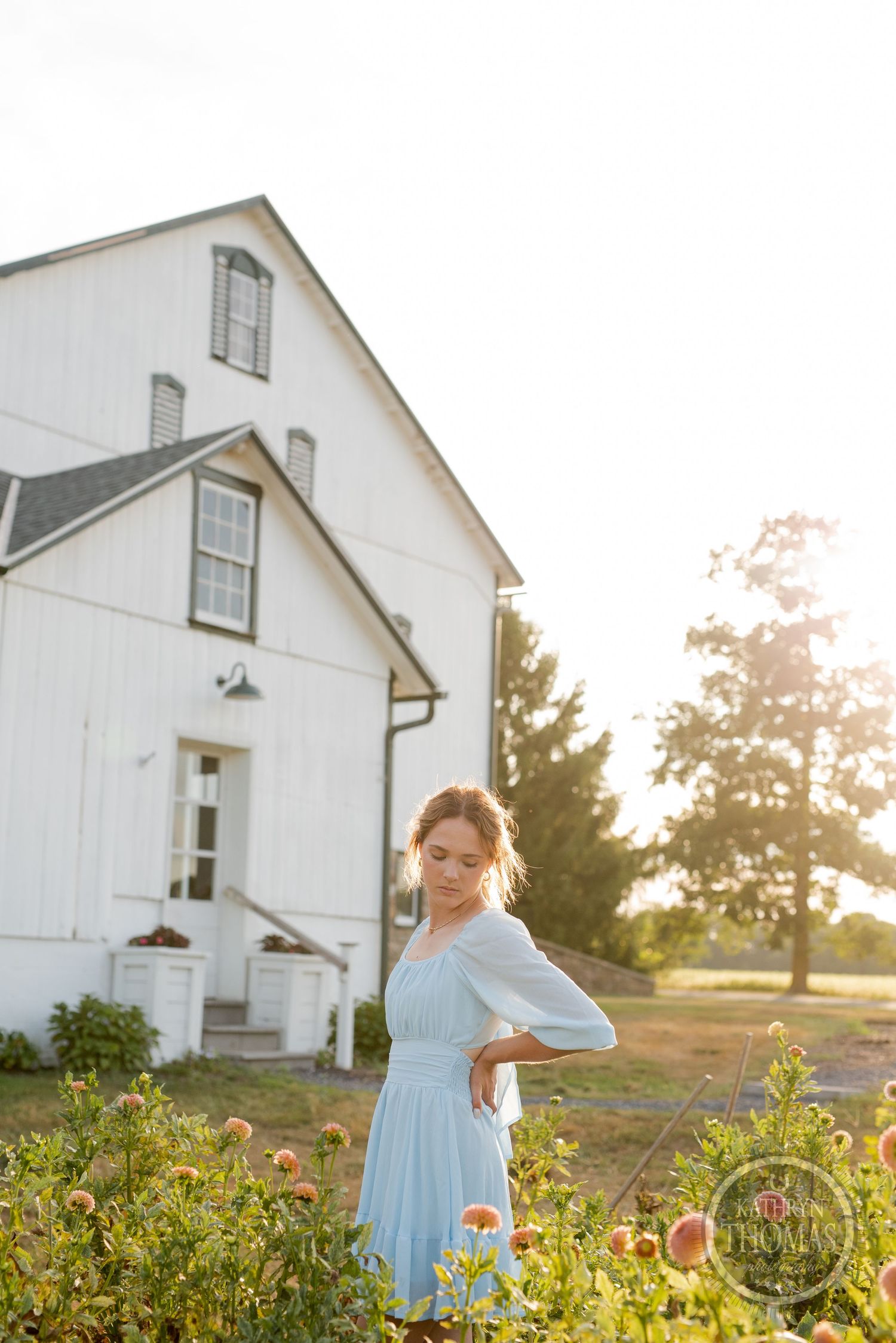 Ethereal portrait against white barn with blooming flower garden at golden hour.