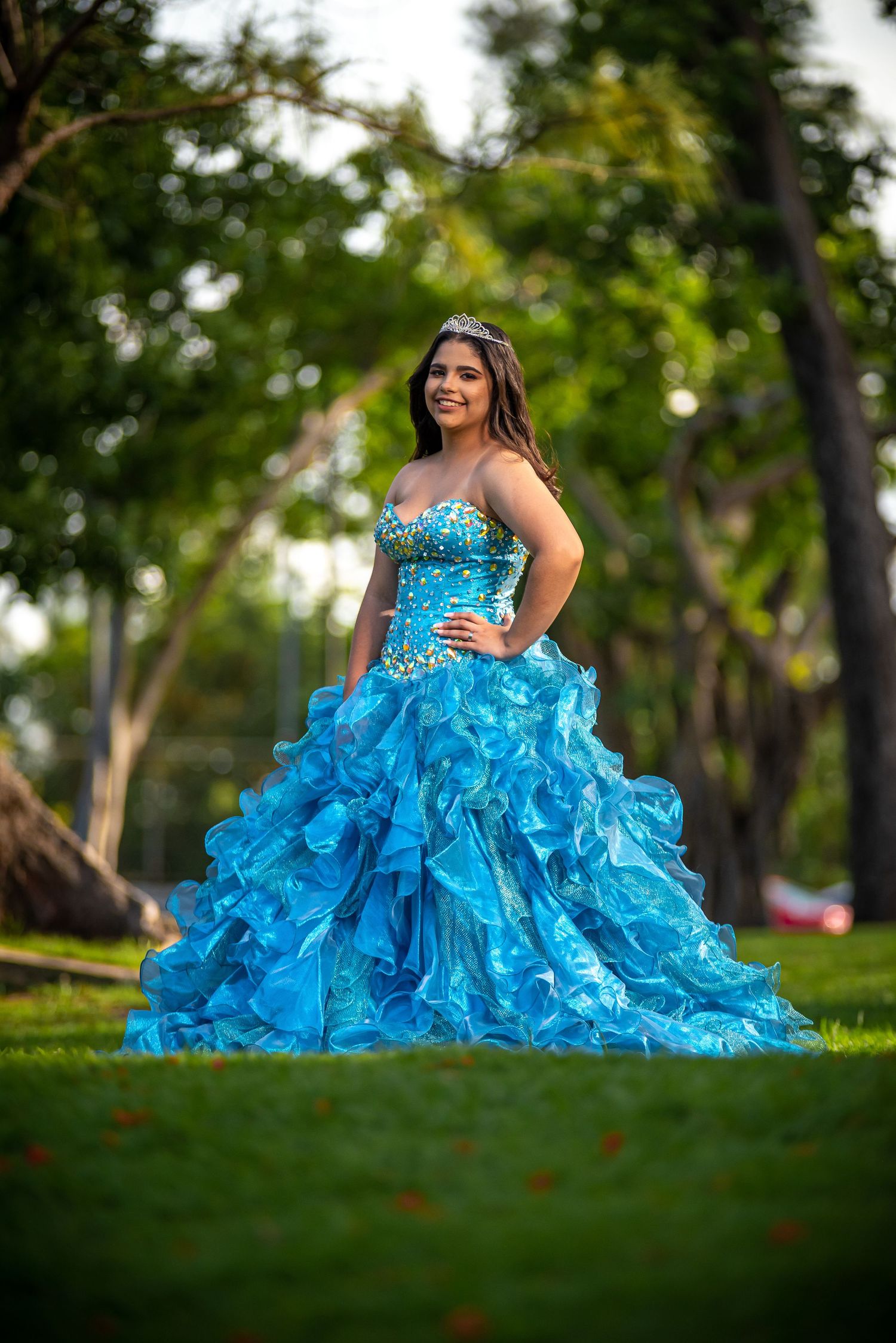 Vibrant turquoise ball gown with ruffled details photographed in an outdoor garden setting.