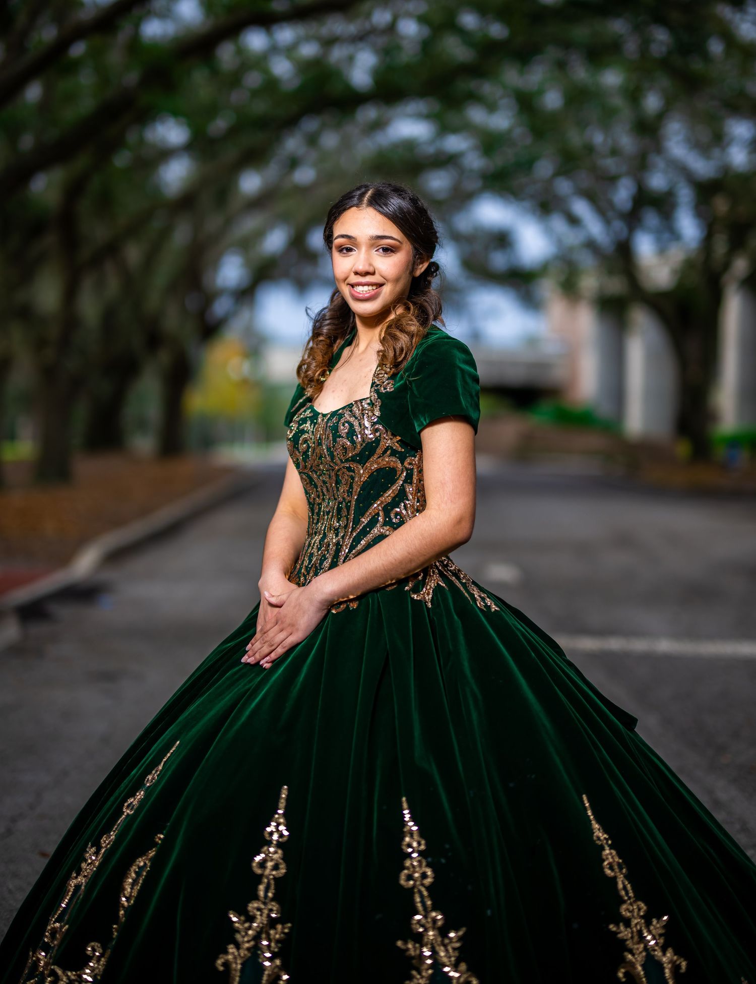 Elegant emerald green ballgown with gold embellishments photographed in an outdoor setting.