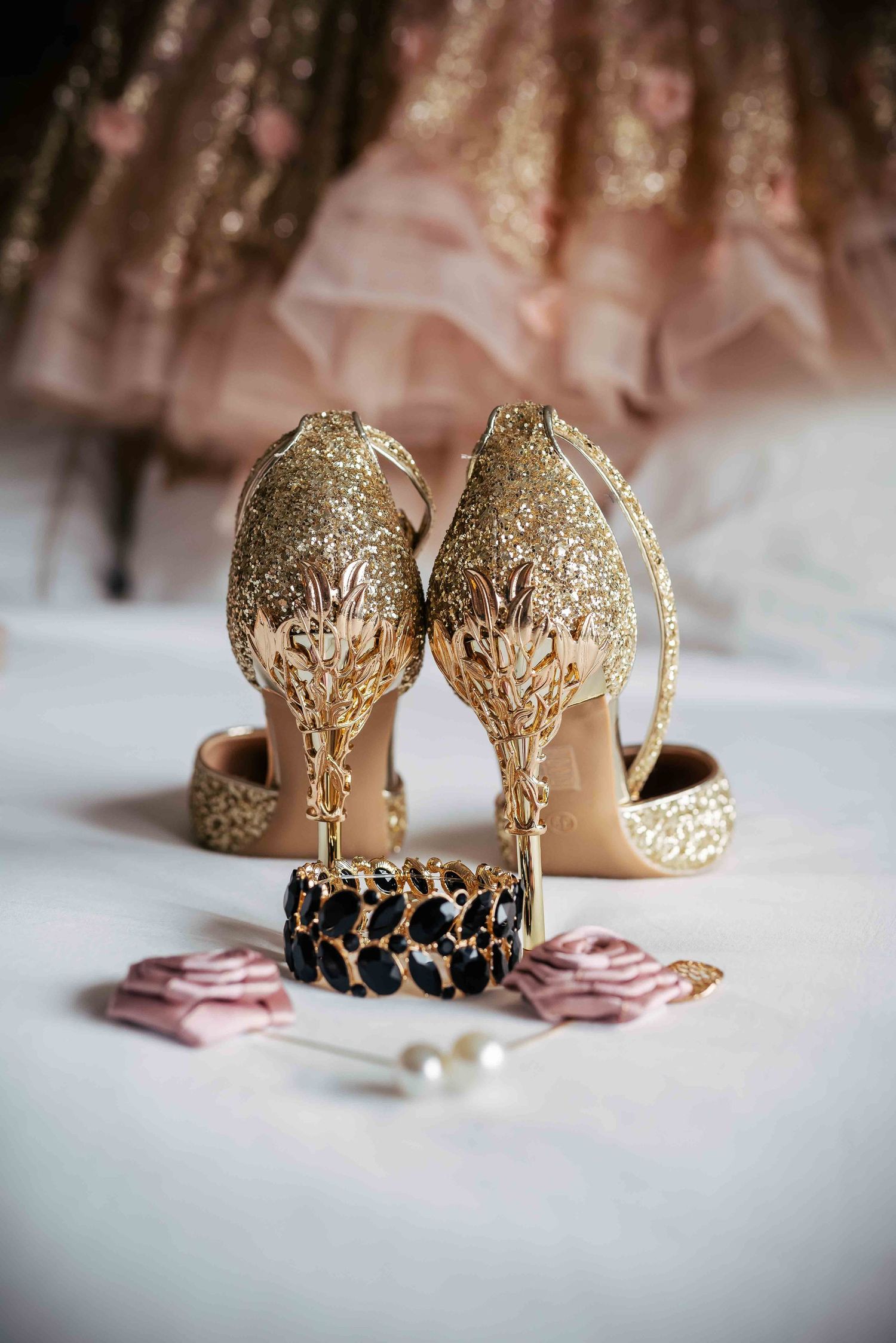 Elegant gold glitter wedding heels with ornate detailing photographed with jewelry.