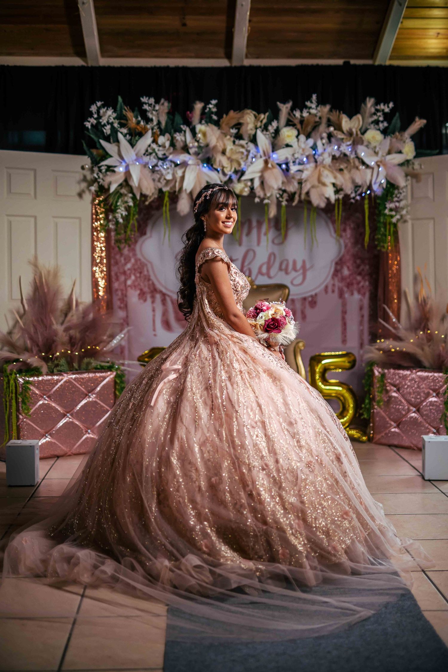 Stunning pink lace quinceañera ball gown under floral archway with party decorations.