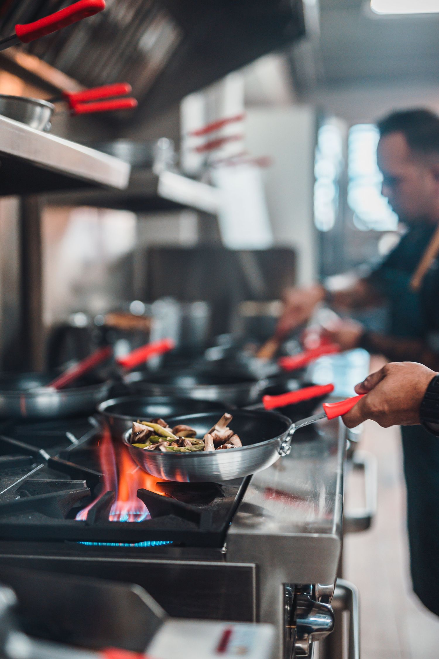Chef cooking with flaming pan on professional gas stove in restaurant kitchen.