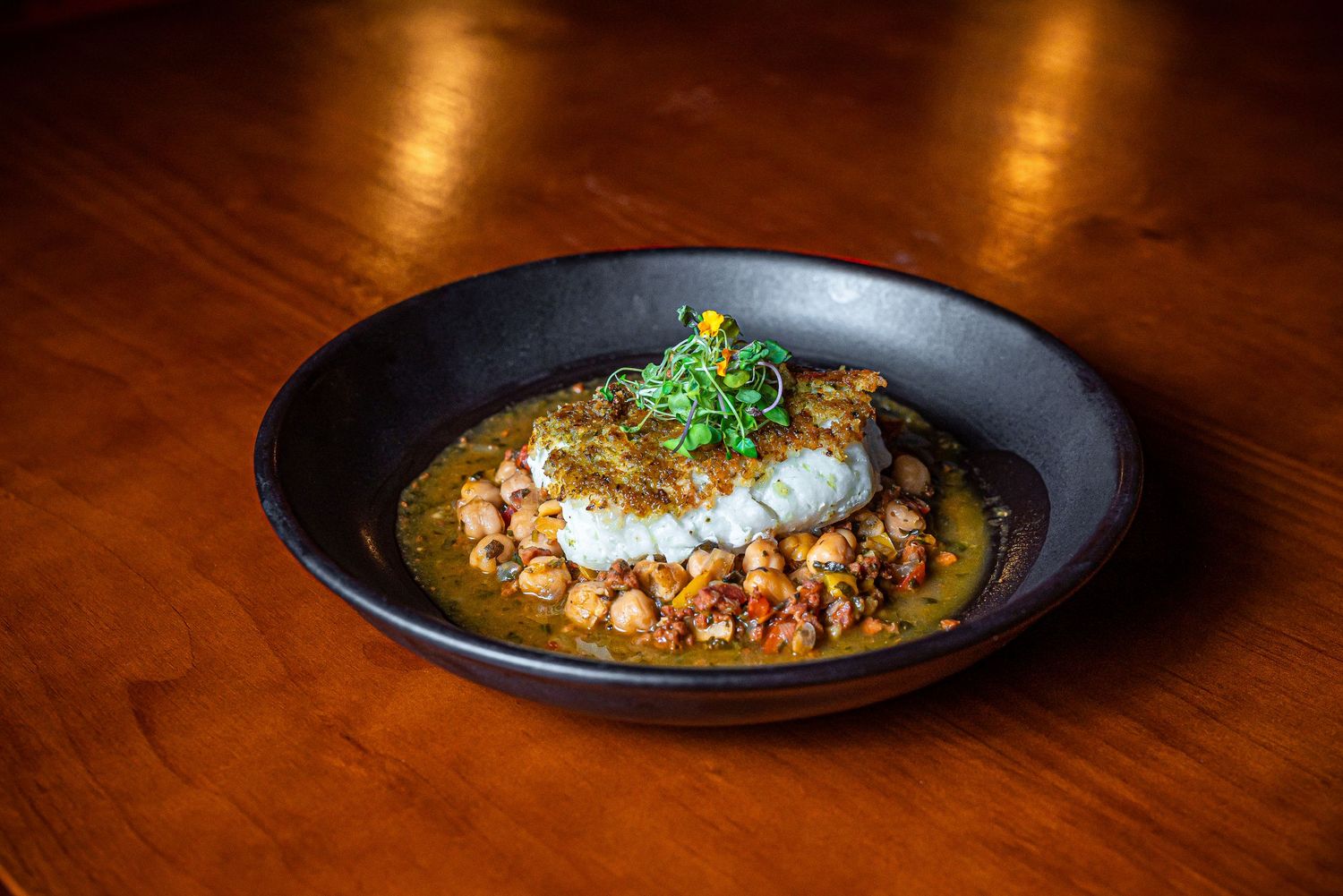 Creamy braised meat dish topped with fresh herbs served in a black bowl on a wooden table.