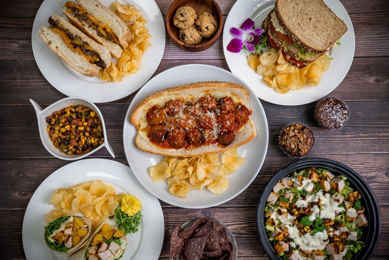 Overhead view of various comfort foods including sandwiches, pasta, and side dishes on wooden table.