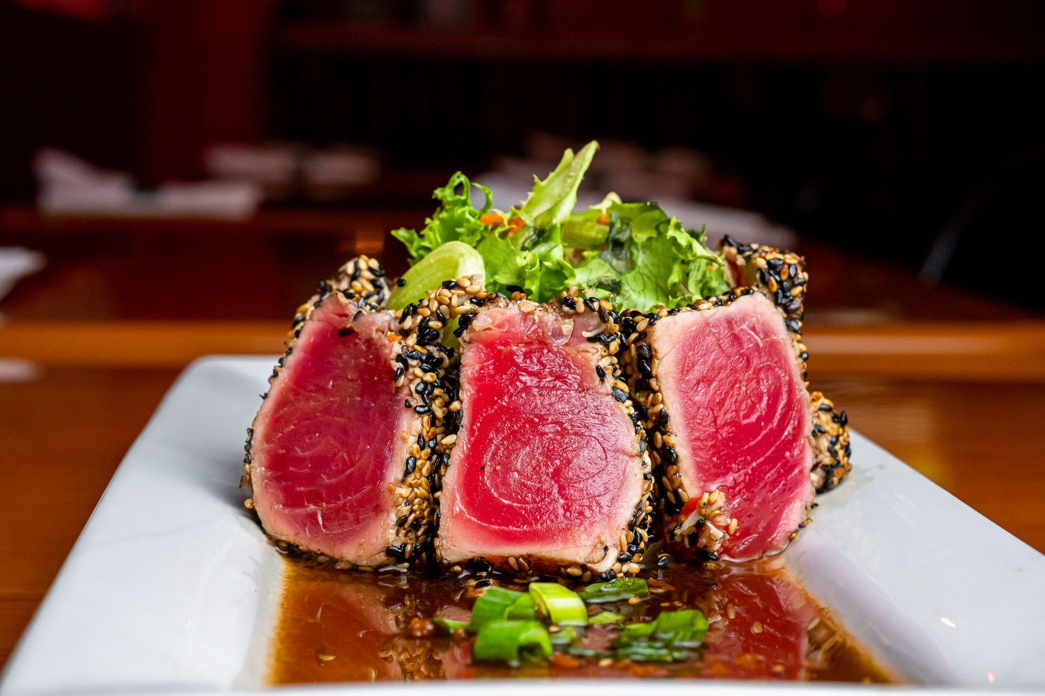 Seared rare tuna steak with sesame crust and microgreens on white plate.