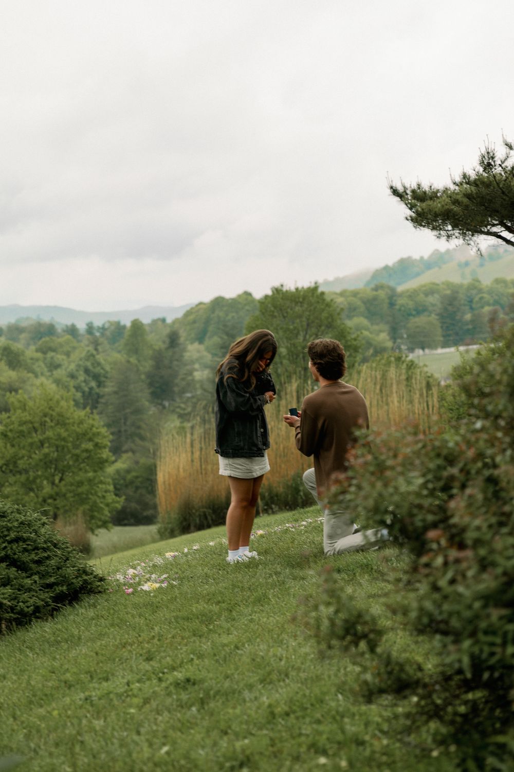 Two people walking on a green hillside with mountains in the background.
