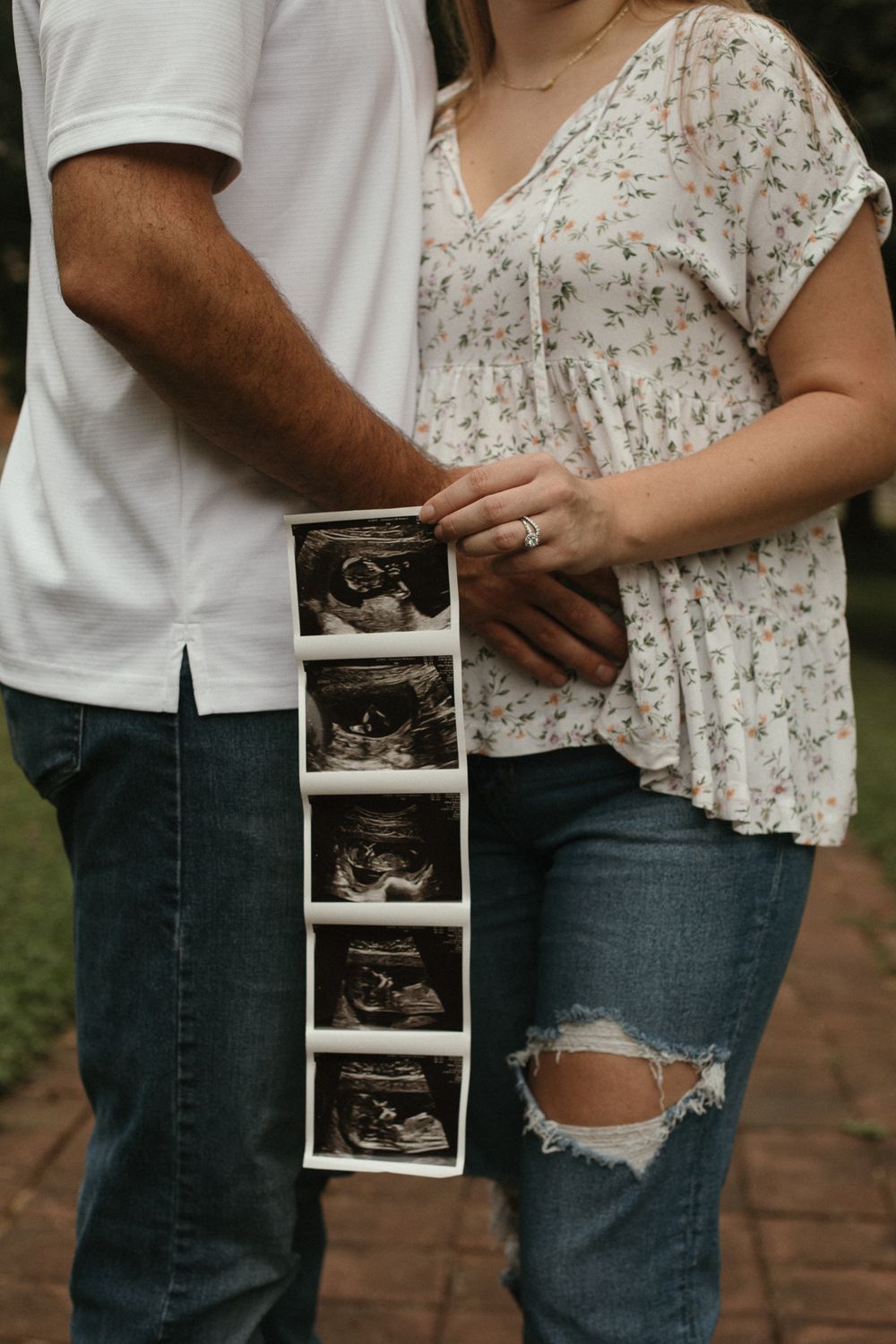 A couple holds ultrasound photos while sharing a pregnancy announcement in casual attire.