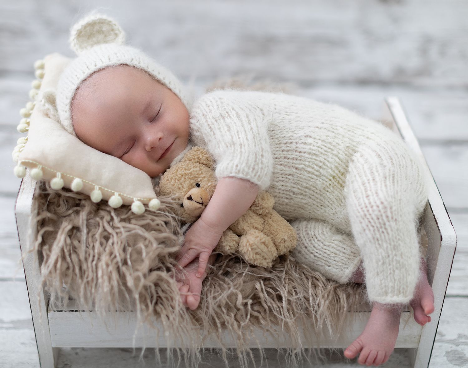 shelly Loxton photography picture of newborn baby in a fluffy romper outfit clothing holding a teddy on a bed.