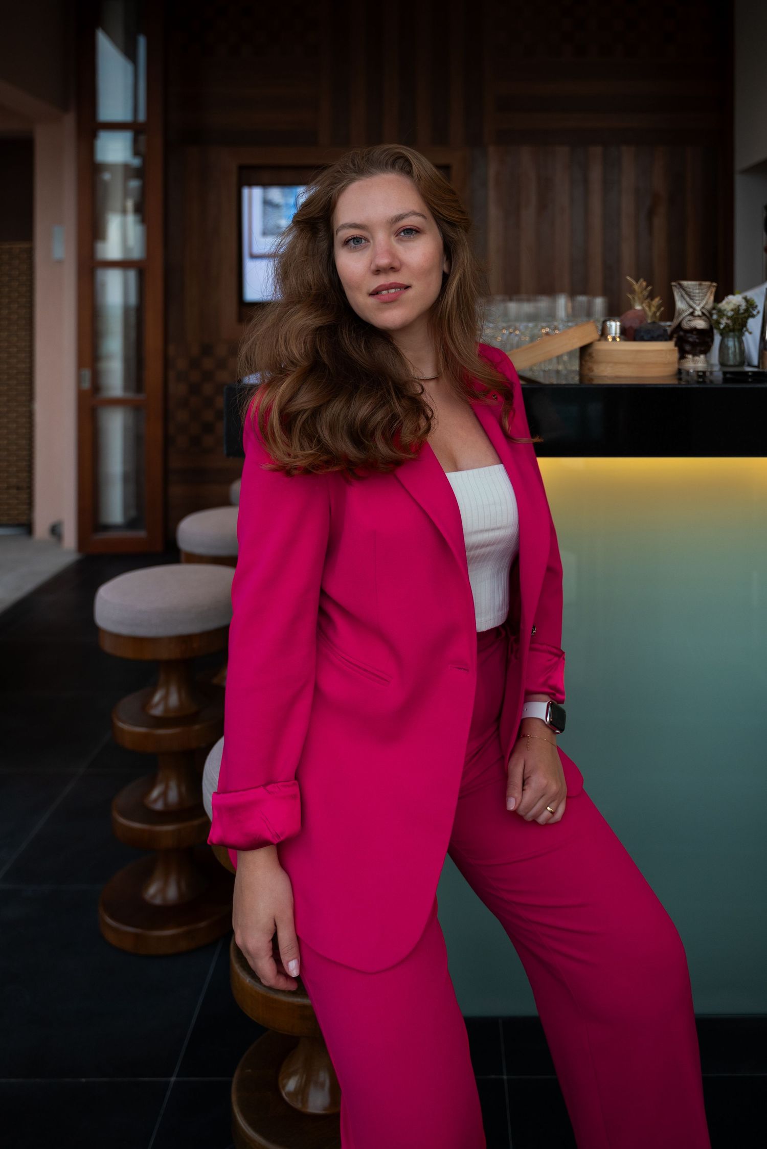 A stylish young woman in a pink suit stands confidently at the bar, exuding elegance and charm