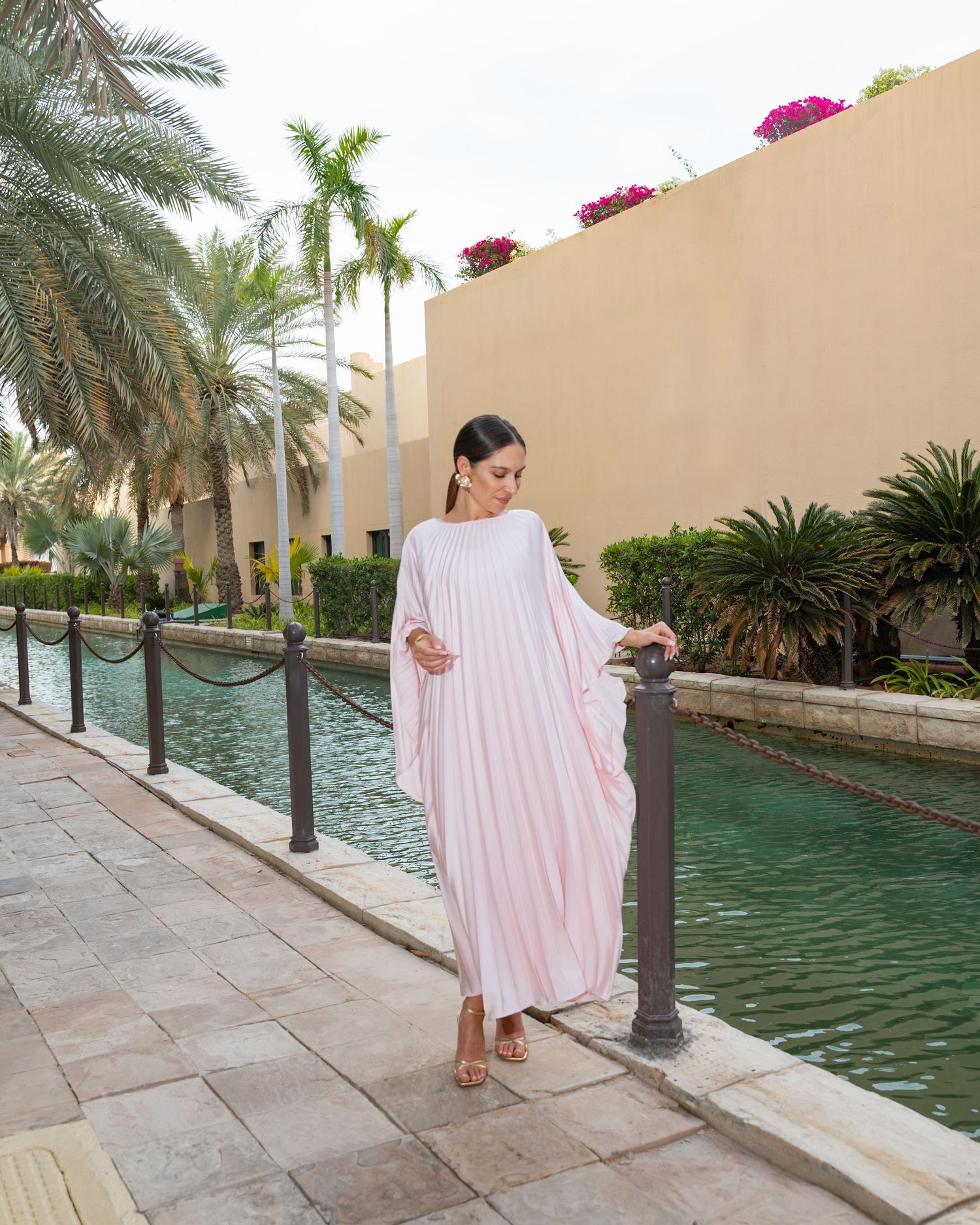 A young woman in a pink abaya stands gracefully, her presence exuding elegance and cultural pride