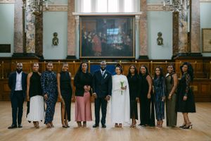A wedding party poses for a formal group photo in an elegant hall with marble columns.