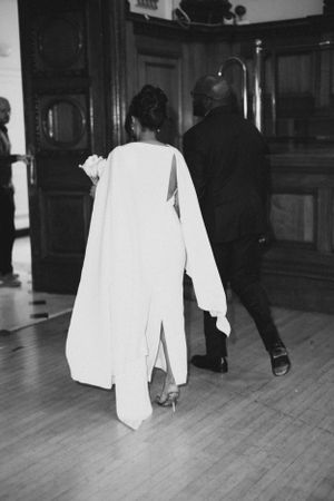 A black and white photo of a couple walking across a wooden floor in formal attire.