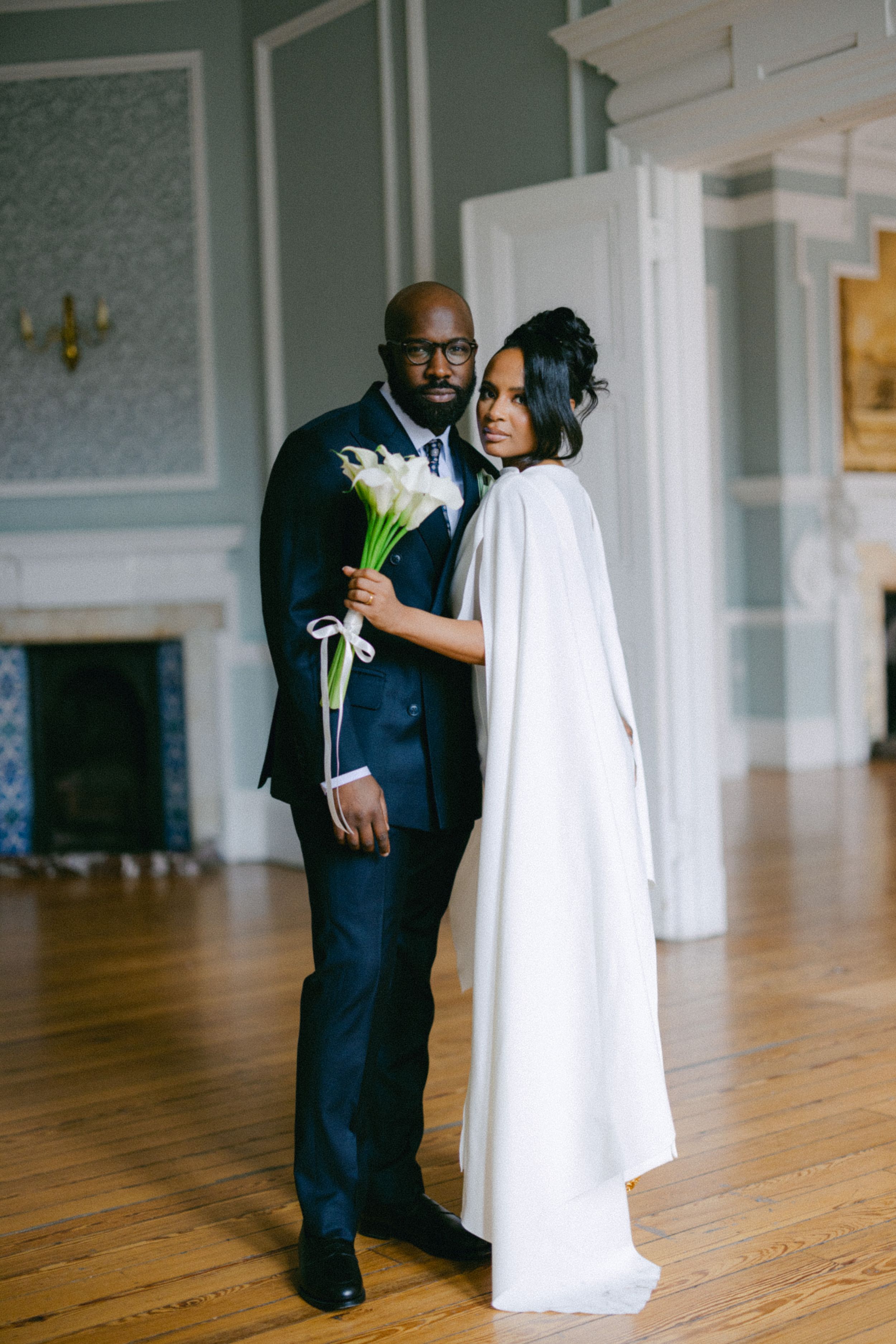 Elegant couple poses with calla lily bouquet in a stately room with mint green walls.