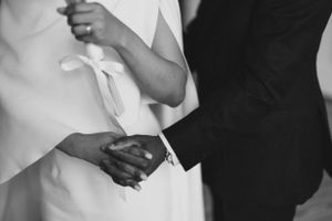 Black and white detail shot of hands holding calla lilies during wedding ceremony.