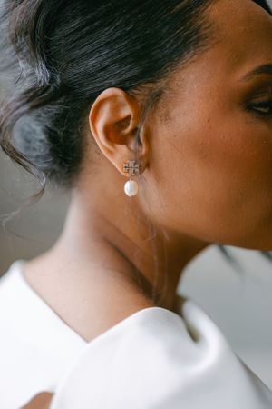 Close-up of pearl drop earring with cross detail on elegant bride.