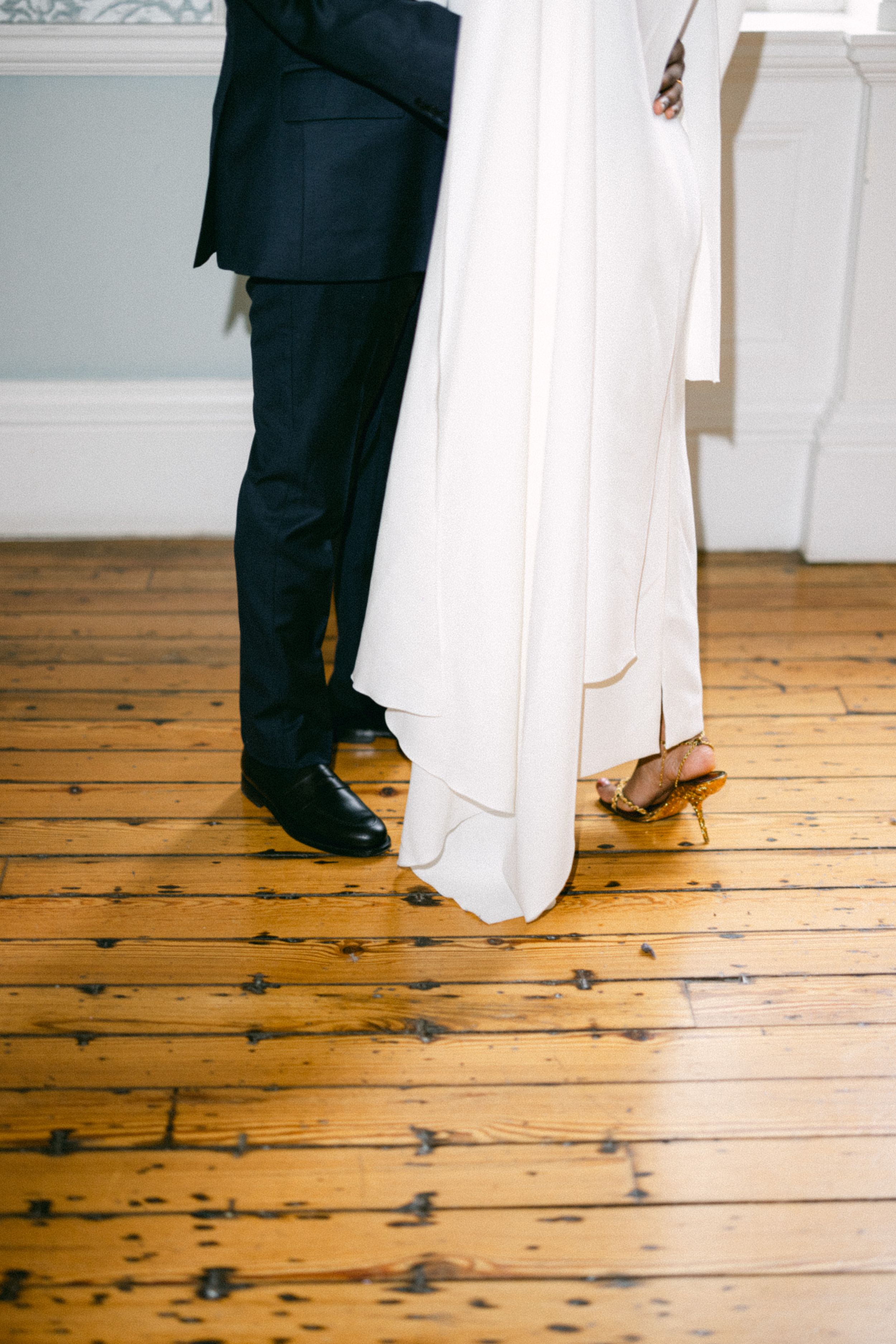 Detail shot of wedding couple's feet and attire against wooden floor.