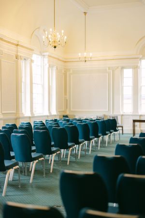 Elegant event space with rows of teal chairs and crystal chandelier.