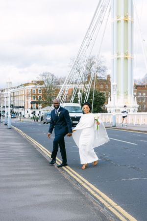 A newlywed couple poses playfully on a bridge with urban architecture in the background.