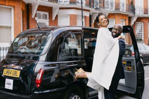 Wedding couple exiting a classic black London taxi cab on their special day.