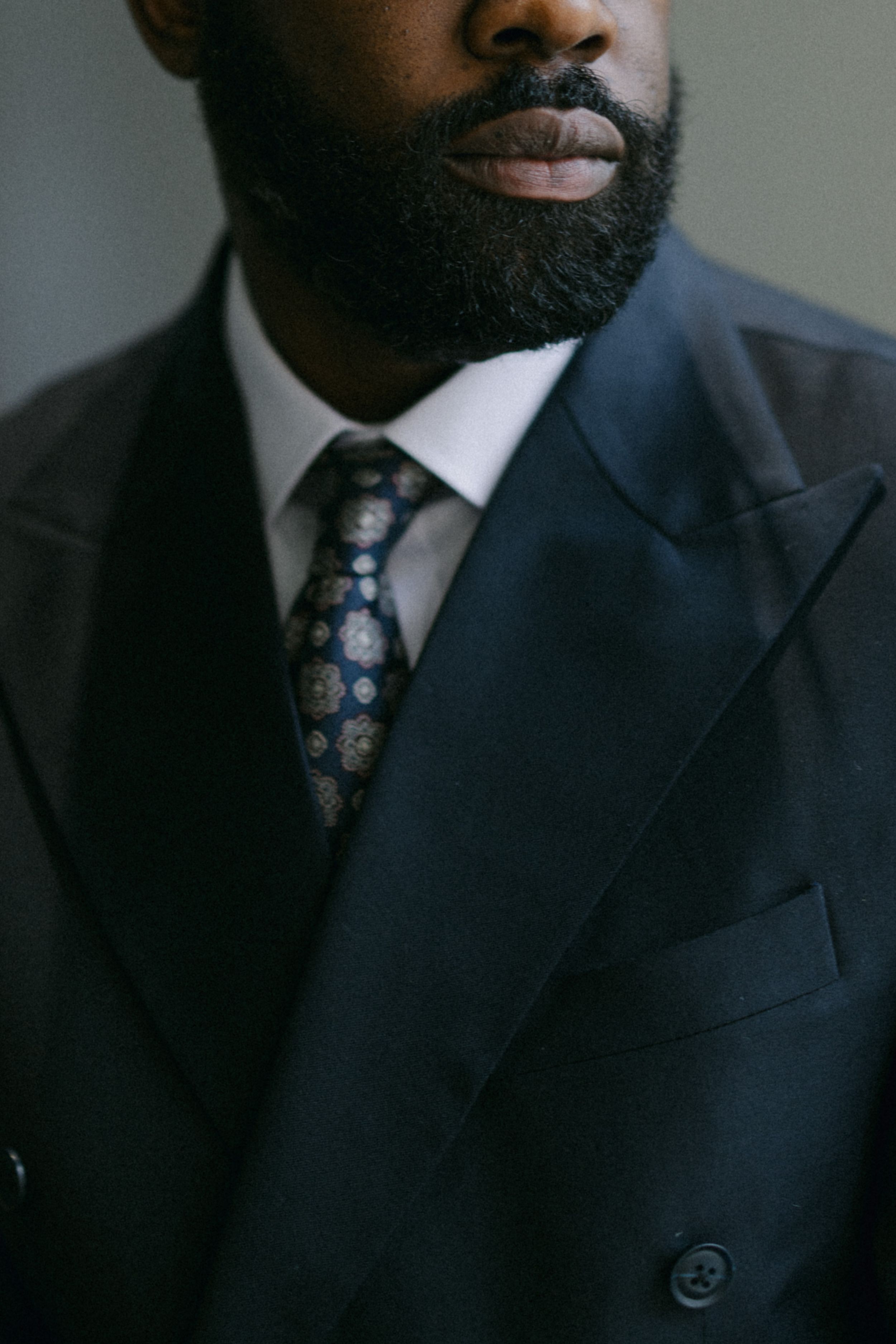 Close-up detail of navy suit jacket with patterned tie and white collar.
