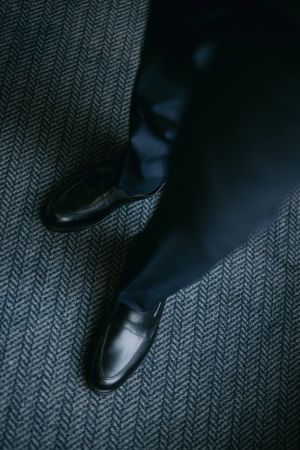 Black leather dress shoes on herringbone patterned carpet in moody lighting.