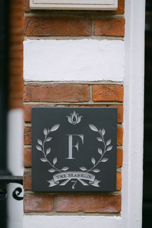 Grey monogram sign with letter F and laurel wreath mounted on brick wall.