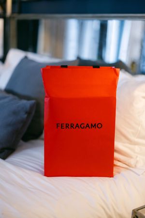 Orange Ferragamo shopping bag sits on white bedding, showcasing luxury retail packaging.