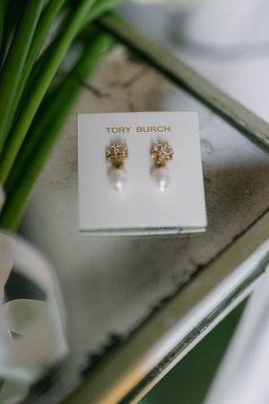 Tory Burch pearl drop earrings displayed on white card with green plant accent.