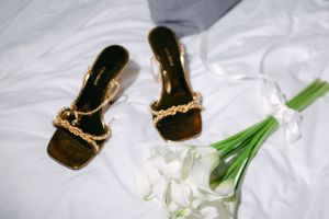 Elegant gold chain sandals displayed next to white calla lilies on white fabric.