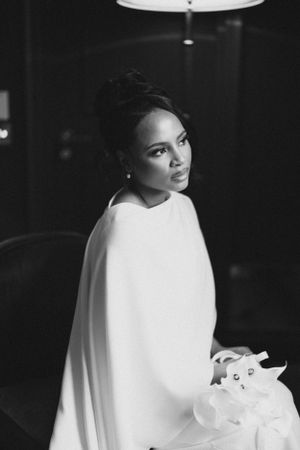 Black and white portrait of bride in elegant cape dress holding bouquet.