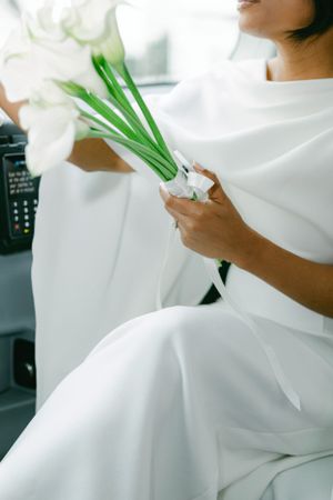 Close-up of white dress detail with green flower stems held in hands.
