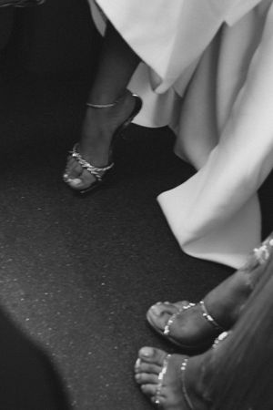 Black and white photo of feet in decorated sandals beneath flowing white fabric.