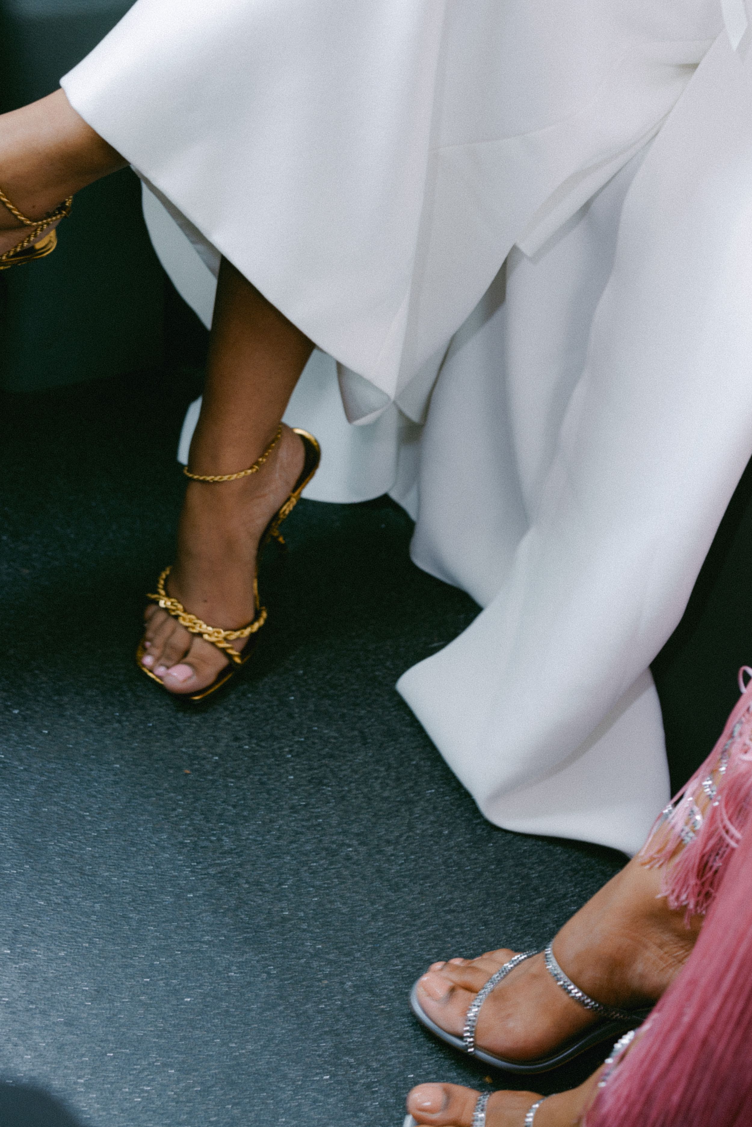 Detail shot of gold chain sandals and white wedding dress hem.