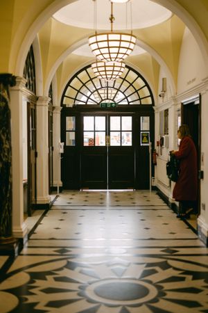 Elegant hallway with arched ceiling, decorative lighting and patterned floor leads to grand entrance doors.
